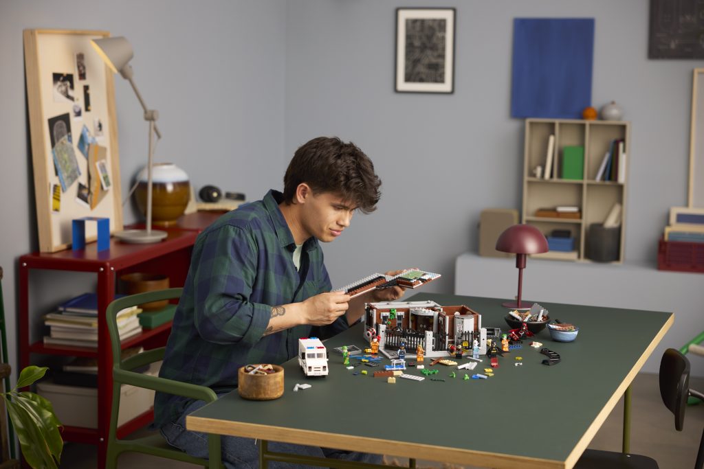 Person focused while building the LEGO Batman Arkham Asylum set at a table with parts and instructions
