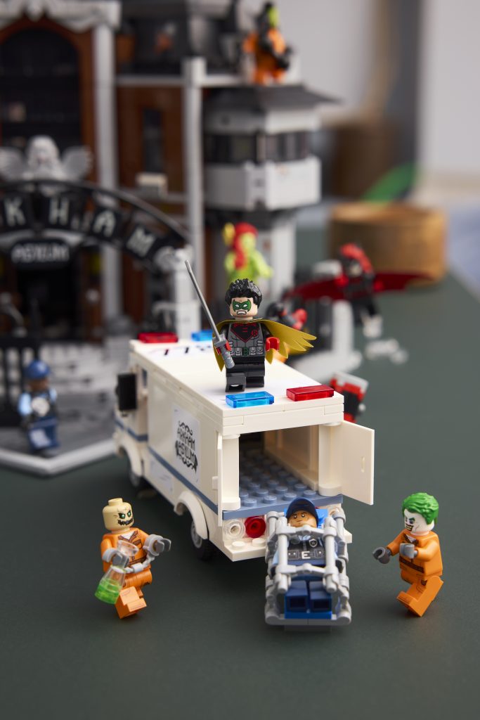 Robin standing atop LEGO Arkham inmate van while Joker, Scarecrow, and guard figures interact below