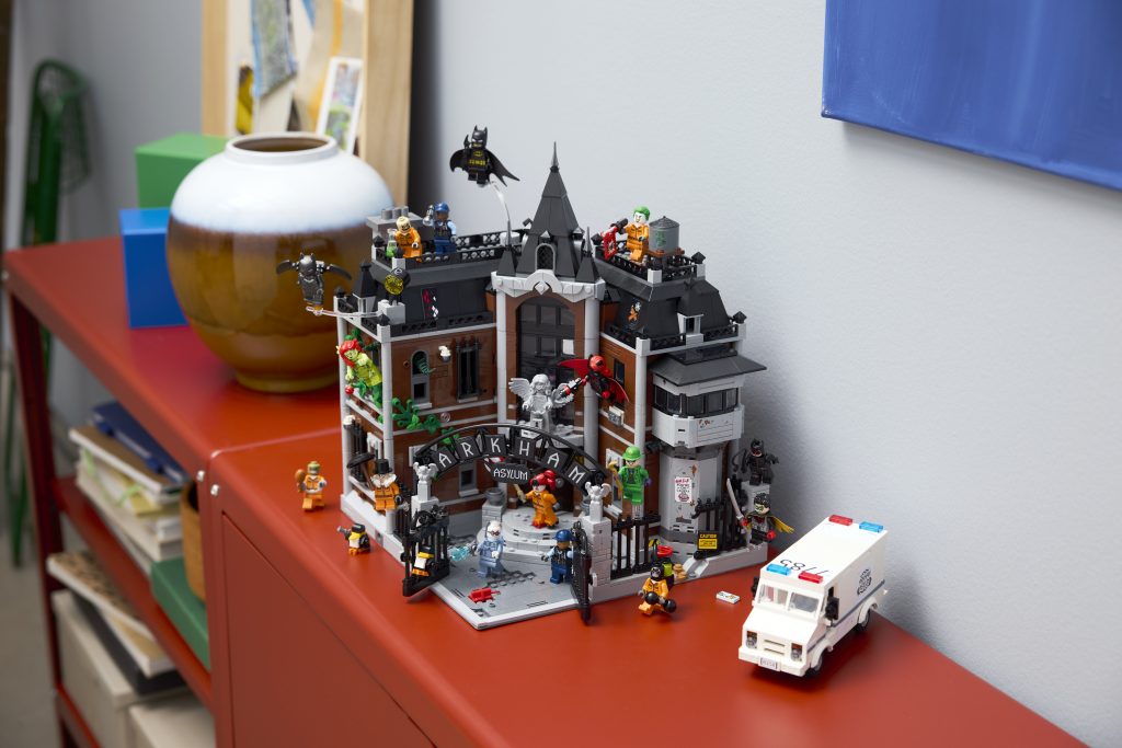 LEGO Batman Arkham Asylum model displayed with minifigures on a red shelf beside a ceramic pot