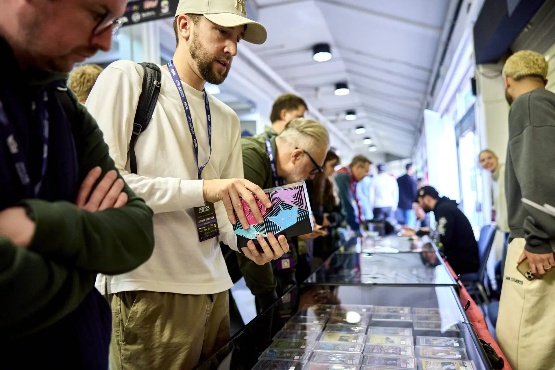 Trading card fans examining sealed boxes and slabs at a long vendor booth at London Card Show