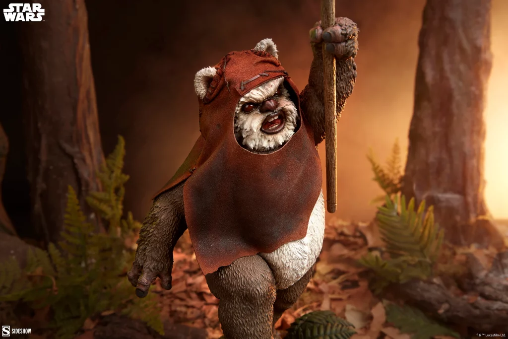 Close-up of Sideshow’s Wicket Premium Format Figure from Star Wars, showing detailed fur, weathered hood, and spear held high in a forest setting with warm lighting
