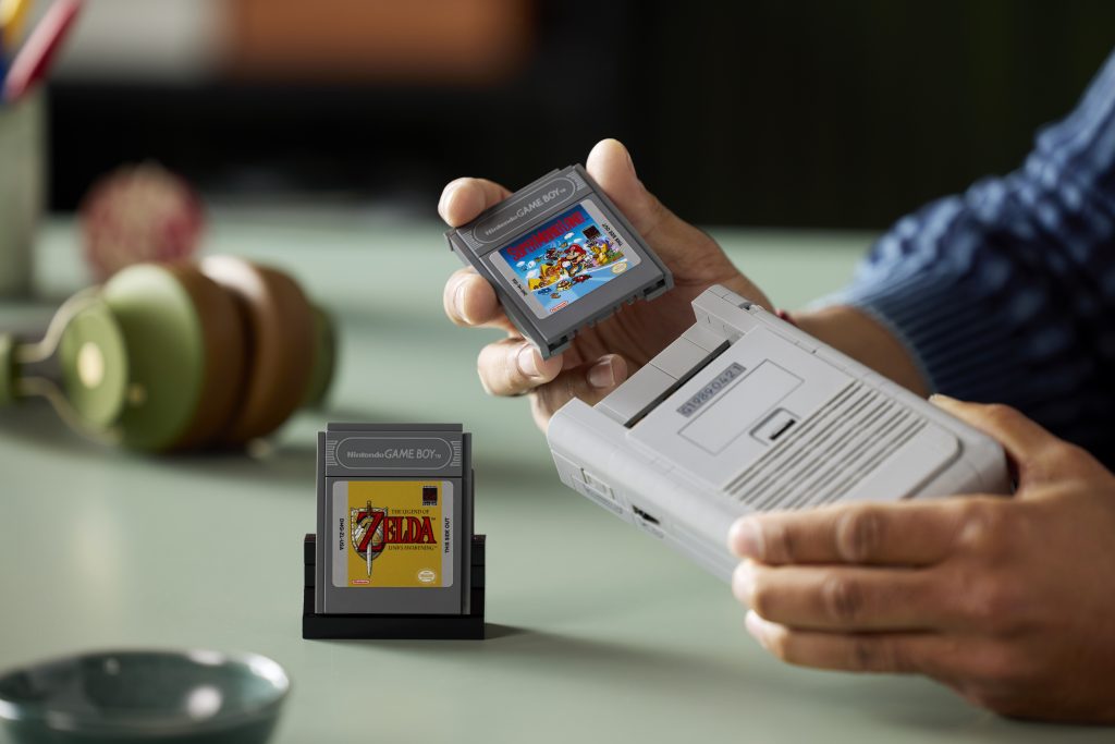 Hands holding LEGO Game Boy model inserting Super Mario Land Game Pak, with Zelda Game Pak on display in foreground